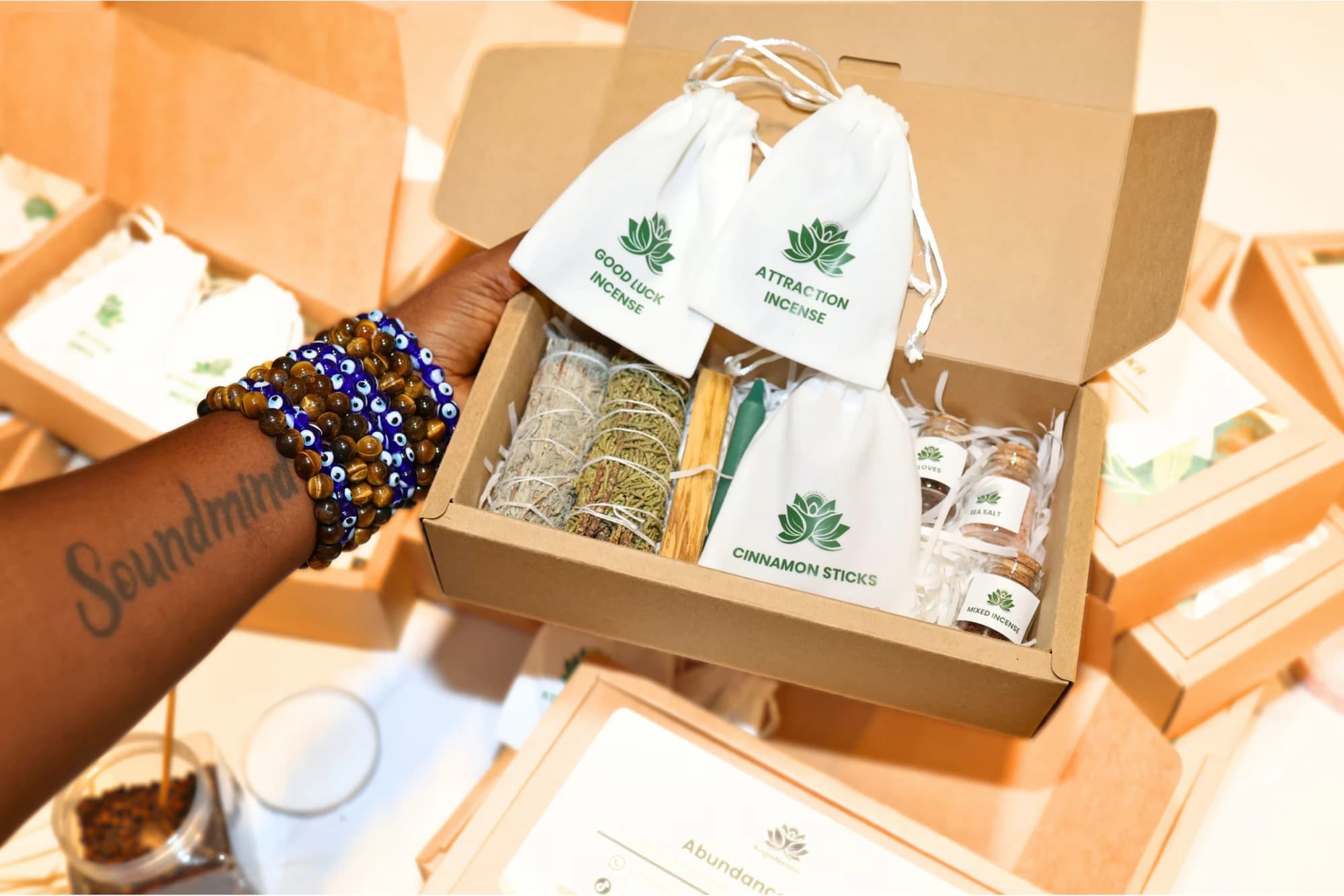 An AngieNation kit box with incense, sage and cinnamon, held by a hand wearing beaded bracelets